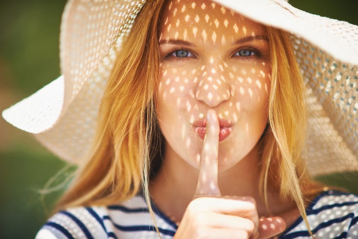 Pretty woman in sunhat looking at camera and making shh gesture